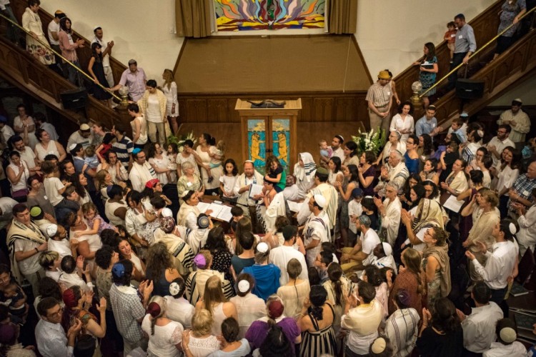 Dozens of people wearing Jewish religious garments gather in a semi-circle around a terbernacle for Kol Tzedek Synagogue's annual Yom Kippur service.